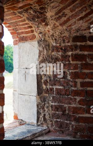 Una finestra ad arco incorniciata in pietra in una roccaforte secolare in mattoni rossi Foto Stock