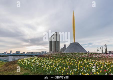 Monumento Golden Spike a Odaiba, Tokyo, Giappone, circondato da tulipani colorati. Lo sfondo moderno della città aggiunge un contrasto urbano alla vibrante primavera Foto Stock