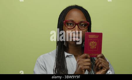 Donna con passaporto russo su sfondo giallo che indossa occhiali e camicia a righe, raffigurante concetti di viaggio e identità. Foto Stock