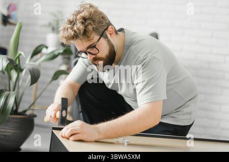 Ritratto dell'uomo che monta mobili. Faccia esso voi stessi l'assemblaggio della mobilia nel paese Foto Stock