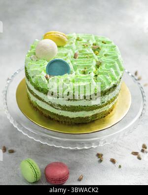 Deliziosa torta al pistacchio con glassa di crema di burro decorata con macaron e pistacchio di noci su un banco per torte di vetro Foto Stock