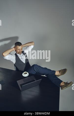 Vista dall'alto di un bel barbuto imprenditore con un elegante baffi, vestito con un abito classico e la camicia bianca è in appoggio a gambe incrociate seduti a Foto Stock