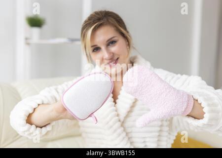Eccitato giovane donna gioiosa ha avvolto la testa in asciugamano che tiene la spugna asciutta dell'acquazzone della spazzola e una procedura di fare della stazione termale Foto Stock