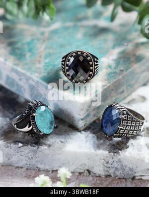 Anelli da uomo in argento con pietre preziose nere, blu e verdi su sfondo turchese Foto Stock