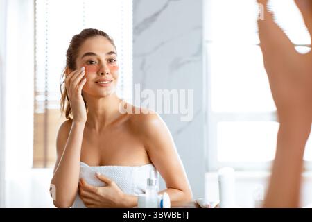 Donna che applica le macchie sotto-occhio pelle idratante sotto gli occhi in bagno Foto Stock