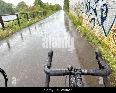 Una strada vista dal punto di vista di un ciclista su una bicicletta in una giornata di pioggia senza mani sul bar Foto Stock