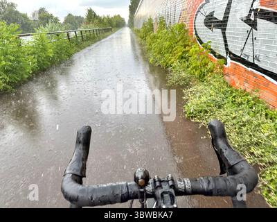 Una strada vista dal punto di vista di un ciclista su una bicicletta in una giornata di pioggia senza mani sul bar Foto Stock