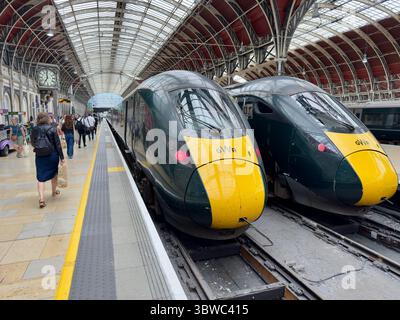 Luglio 2025 due treni GWR fianco a fianco alla stazione di Londra Paddington in prima serata mentre i pendolari camminano lungo la piattaforma per salire a bordo di un treno Foto Stock