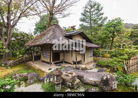 Tradizionale casa giapponese con tetto in paglia accoccolata in un sereno giardino. Lanterne in pietra e rocce coperte di muschio esaltano l'atmosfera tranquilla. Kyoto Foto Stock