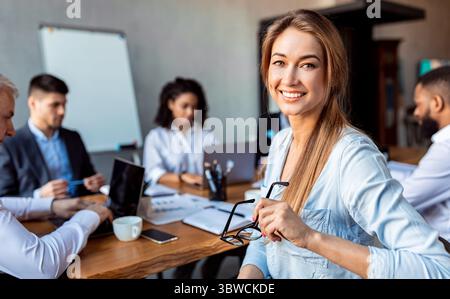 Donna d'affari sorridente seduta in riunione con i colleghi in ufficio Foto Stock