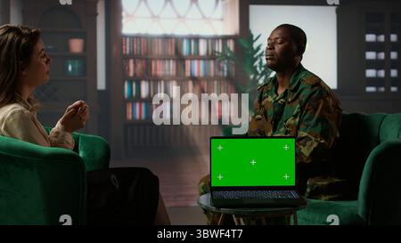 Il personale militare discute con un terapeuta accanto allo schermo cromatico, che soffre di PTSD dopo scene di combattimento horror. La counselor donna offre aiuto e sostegno al soldato afroamericano. Telecamera A.. Foto Stock
