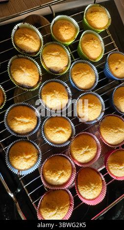I cupcake dorati si raffreddano su una griglia metallica, appena sfornati in carta colorata. I cupcake presentano una parte superiore perfettamente arrotondata, che mostra un appetitoso Foto Stock