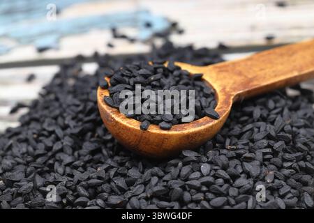 Semi di cumino nero e olio essenziale con ciotola e pala o cucchiaio di legno. Nigella Sativa in bottiglia di vetro. Medicina di erbe organica per molte malattie Foto Stock