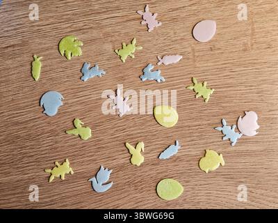 Varie forme di carta colorata, tra cui conigli e uova, sparse su una superficie di legno. I colori pastello brillanti creano un divertimento e una festa Foto Stock