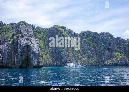Barche locali che navigano lungo l'oceano, portando i viaggiatori da El Nido a visitare le isole di Palawan. Le bellissime acque blu con scogliere calcaree Foto Stock