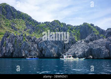 Le barche locali navigano lungo l'oceano, portando i viaggiatori del tour di El Nido a visitare le isole di Palawan. Le bellissime acque blu con scogliere Foto Stock