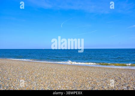 Spiaggia di ghiaia che incontra il mare sotto un cielo blu vivace. Thorpeness Shingle Beach, Suffolk, Inghilterra. Foto Stock