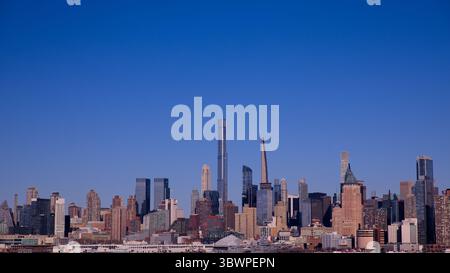 La luce del sole mattutina bagna l'iconico skyline di Manhattan da Jersey City attraverso il fiume Hudson, catturando il vibrante panorama sul lungomare di New York. Foto Stock