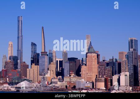 Lo skyline di Manhattan illuminato dal sole si erge sopra il fiume Hudson da Jersey City, mostrando gli scintillanti grattacieli di New York sotto un cielo blu cristallino e vibrante! Foto Stock