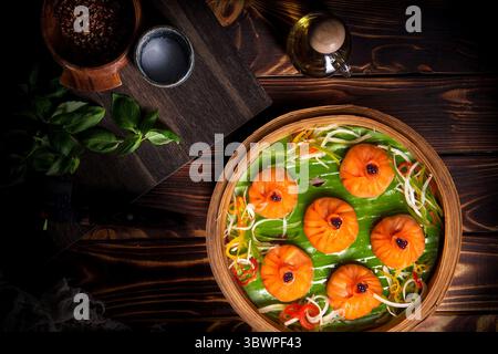 Deliziosi gnocchi al vapore color arancia serviti su una foglia di banana con verdure grattugiate e guarniti con salse. Una vivace e gustosa delicatezza asiatica Foto Stock