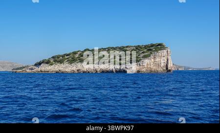 Isola rocciosa con scogliere ripide e vegetazione sparsa nell'arcipelago di Kornati, circondata dal blu profondo del mare Adriatico sotto il cielo estivo. Foto Stock