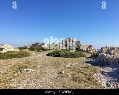 Rovine di antichi edifici in pietra su una collina rocciosa a Murter-Kornati, contea di Sibenik-Knin, Croazia, sotto un cielo azzurro e limpido in una giornata di sole. Foto Stock