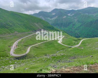 Strada panoramica tortuosa attraverso i verdi Carpazi vicino ad Arefu, contea di Argeș, Romania, sotto un cielo estivo nuvoloso. Foto Stock