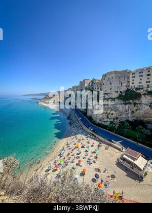 Vista aerea di una spiaggia di Tropea, Italia, con ombrelloni colorati, mare turchese ed edifici sulla cima di ripide scogliere costiere. Foto Stock