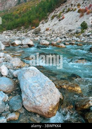 Il limpido fiume di montagna scorre su rocce colorate in un letto di pietra, circondato da colline boscose e rocciose nel nord dell'Albania. Foto Stock