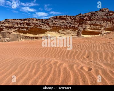Dune di sabbia rossa ondulata e formazioni rocciose a strati sotto un cielo azzurro cristallino nel deserto di Wadi Rum, Governatorato di Aqaba, Giordania. Foto Stock