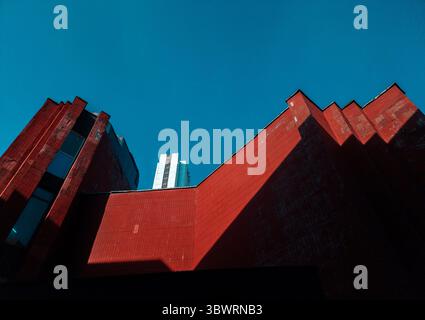 Vista ad angolo basso degli edifici rossi brutalisti che circondano un moderno grattacielo bianco sotto un cielo blu profondo Foto Stock