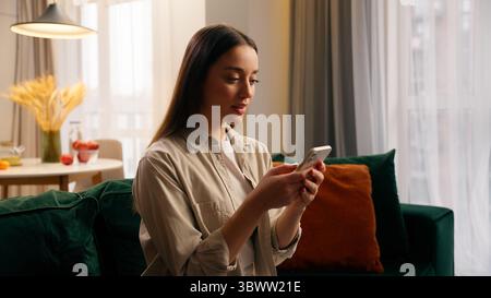 Donna caucasica che utilizza il telefono cellulare a casa ragazza concentrata che chatta messaggi di testo chat smartphone servizio di prenotazione ordine consegna cibo in vita Foto Stock