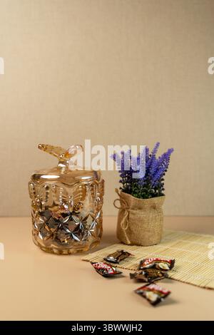 Giacarta, Indonesia, 17 luglio 2025: Vaso decorativo di caramelle in vetro ambrato con coperchio a farfalla, caramelle per caffè e lavanda su un tappetino in bambù. Foto Stock
