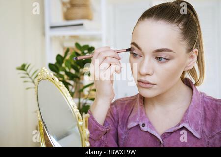 Trucco a casa. La giovane bella donna con il pennello per il trucco applica l'ombra degli occhi Foto Stock