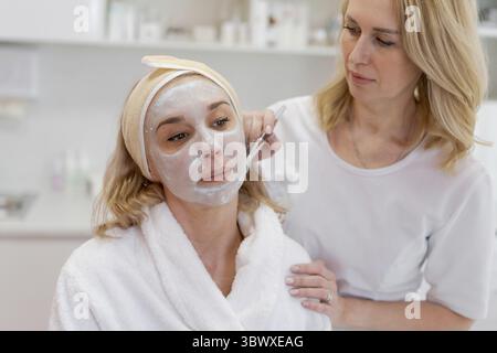 Maschera peeling viso, beauty spa, cura della pelle. Donna che riceve un trattamento viso da estetista presso il salone SPA, vista laterale, primo piano. Trattamento anti-età. COSME Foto Stock