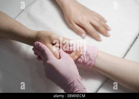 Primo piano mani estetista, le mani della donna ricevono trattamento manicure, master fa un massaggio mano in un salone di bellezza. Concetto di cura delle unghie e delle mani del centro benessere Foto Stock