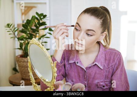 Trucco a casa. La giovane bella donna con il pennello per il trucco applica l'ombra degli occhi Foto Stock