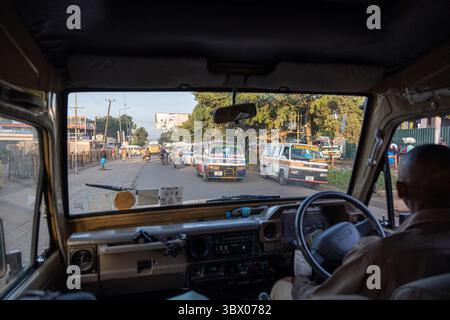 Una vista dal cruscotto di un veicolo mostra una strada cittadina vicino a Manyara, con minibus parcheggiati, volante e strumenti nel telaio Foto Stock