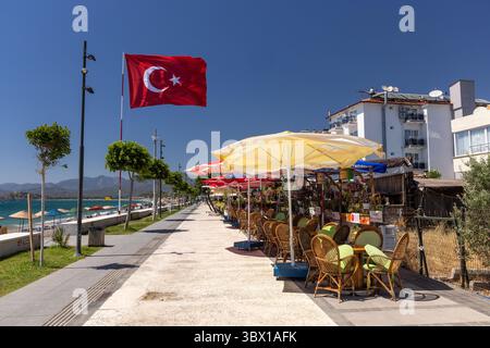 Calis, una popolare località balneare vicino a Fethiye, ha una lunga passeggiata lungomare costeggiata da negozi, bar e ristoranti. Bandiera turca in volo, Mugla, Turchia Foto Stock