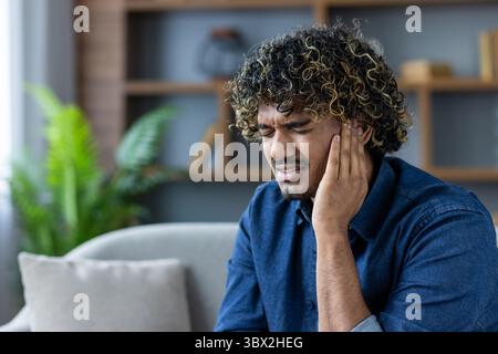 Un uomo dai capelli ricci tiene l'orecchio, visibilmente soffrendo. Sembra che stia avendo un mal di testa o un disagio correlato. Foto Stock