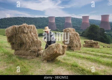 Agricoltore che impilava a mano balle di fieno vicino alle torri di raffreddamento della centrale elettrica di Ironbridge in Gran Bretagna Foto Stock