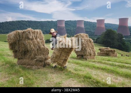 Agricoltore che impilava a mano balle di fieno vicino alle torri di raffreddamento della centrale elettrica di Ironbridge in Gran Bretagna Foto Stock