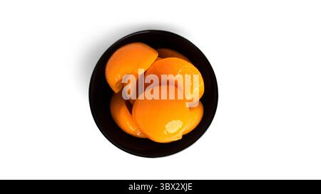 Pesche in scatola in una ciotola nera. Pesche dolci sciroppate isolate su fondo bianco. Foto di alta qualità Foto Stock