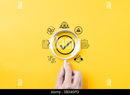 Concetto di garanzia di qualità e certificazione di conformità. Lente d'ingrandimento focalizzata sul segno di spunta con icone di qualità, checklist e conformità, Foto Stock