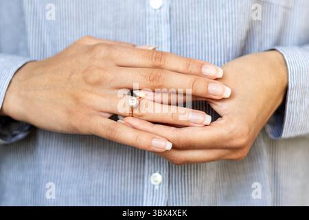 Donna che indossa l'anello di innesto sul primo piano delle dita. Primo piano di una donna che tiene delicatamente il dito con un anello di fidanzamento diamantato, simbolo Foto Stock