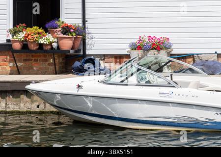 Mostra di fiori colorati in pentole all'esterno di una casa galleggiante con una barca a motore sul fiume Foto Stock