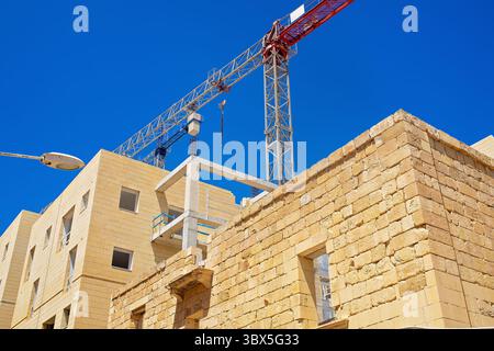 Un edificio in costruzione fatto di blocchi di pietra calcarea con aperture delle finestre, un telaio in cemento e pavimenti non finiti. È visibile una gru da cantiere Foto Stock