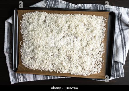 Noce di cocco grattugiato su una teglia rivestita di pantalone: Noce di cocco grattugiata addolcita su una teglia rivestita di carta da forno Foto Stock
