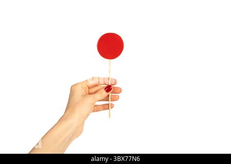 Lecca lecca rotonda con mano femminile isolata su sfondo bianco. Manicure rossa. Chupa Chups. Foto Stock