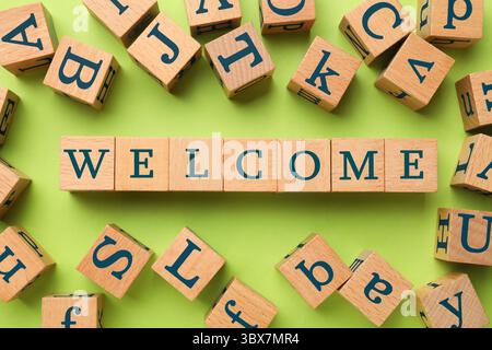 Parola di benvenuto in cubi di legno su sfondo verde chiaro, piano Foto Stock